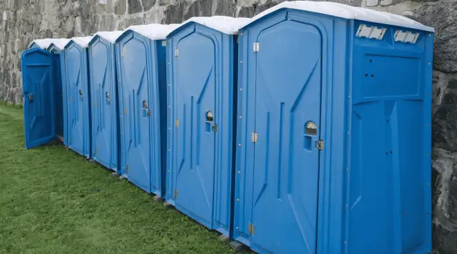 Row of blue portable toilets lined up on grass against a stone wall for event sanitation in Glendale, AZ