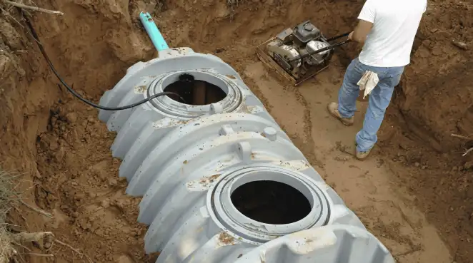 Septic tank installation showing a technician compacting soil around a new poly septic tank in an excavation pit in Glendale, AZ